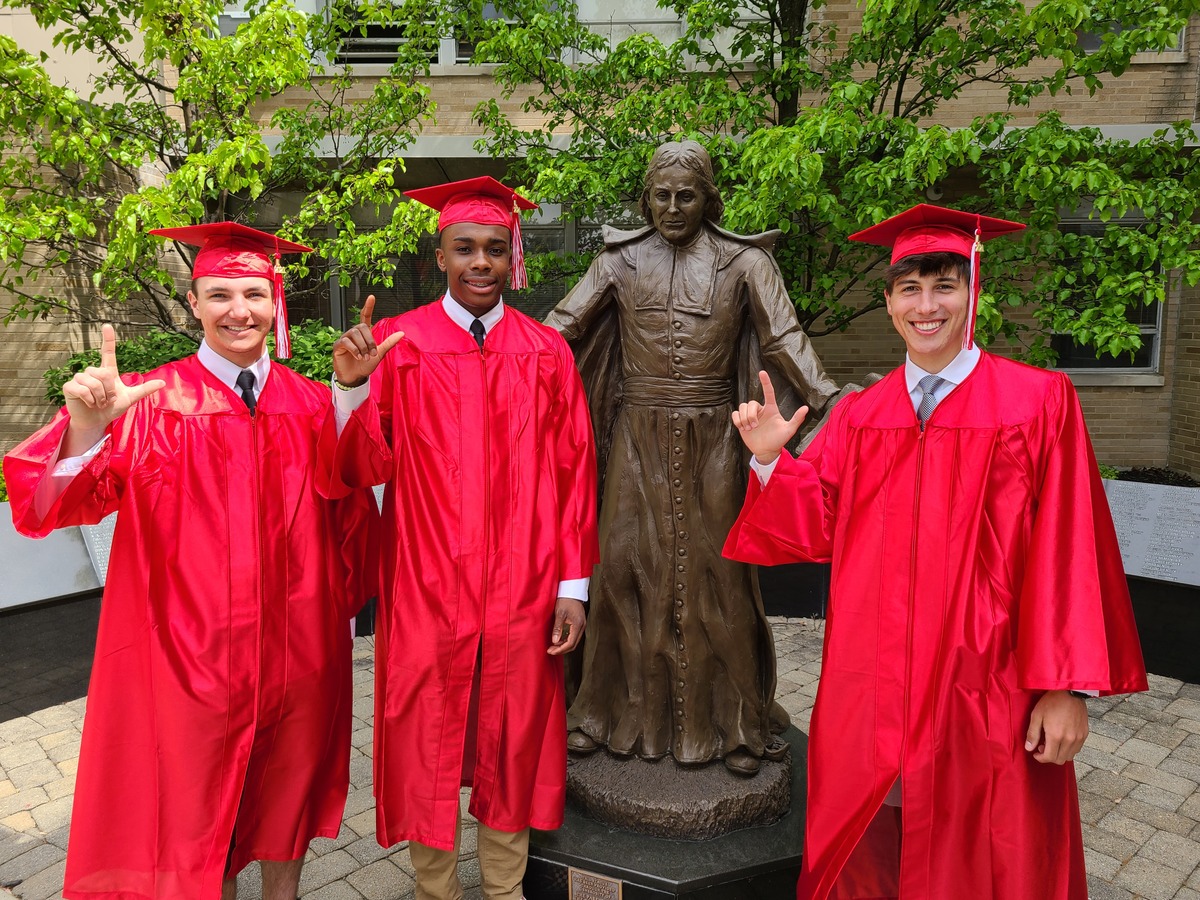 Three men in cap and gown by statue